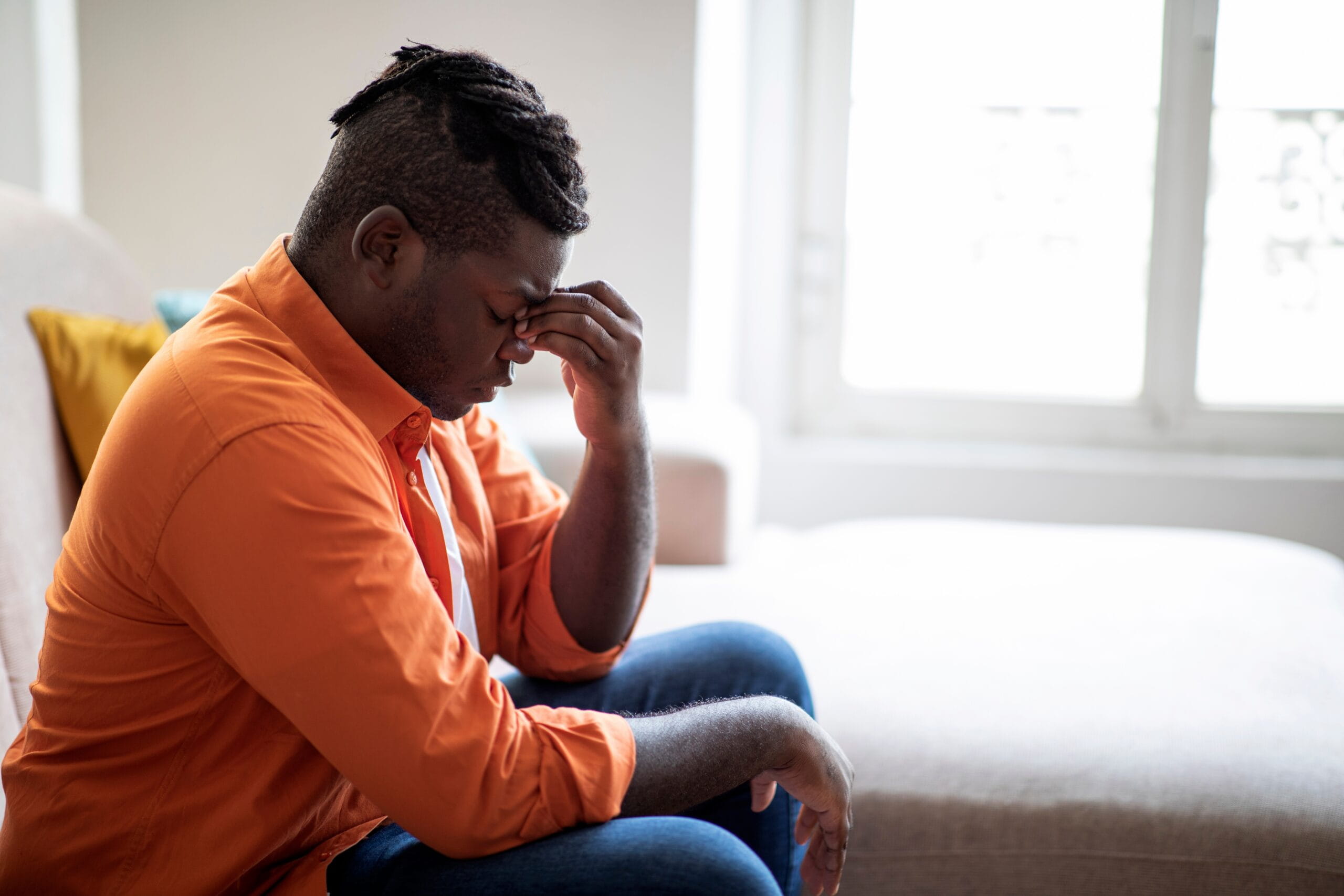 A man sitting on a couch while holding his forehead in pain to soothe a headache and dizziness