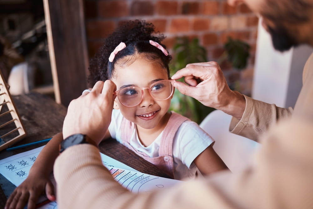 A young girl smiling while her father places new glasses on her