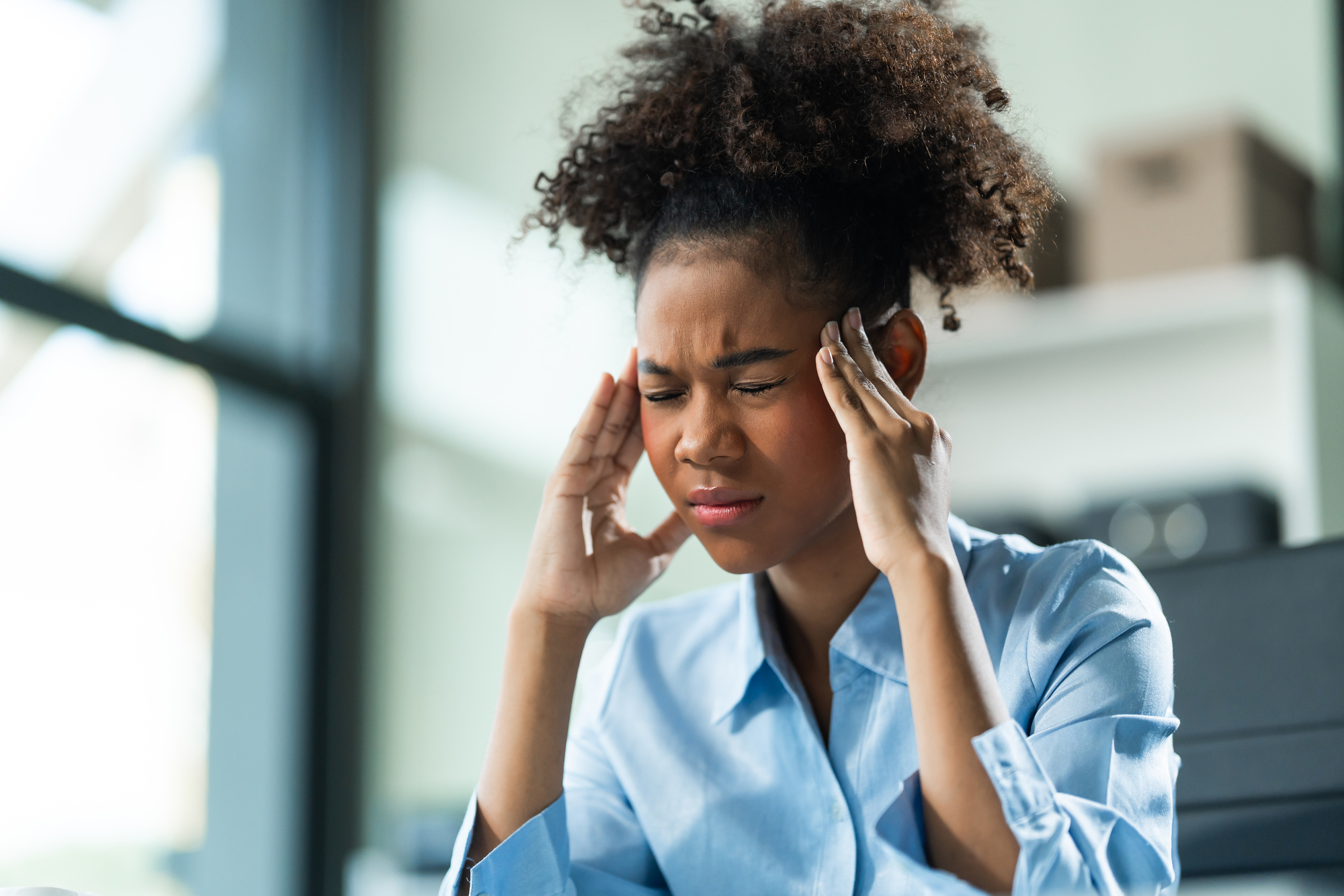 A young African American woman with Afro brown hair in a modern office experiencing panic
