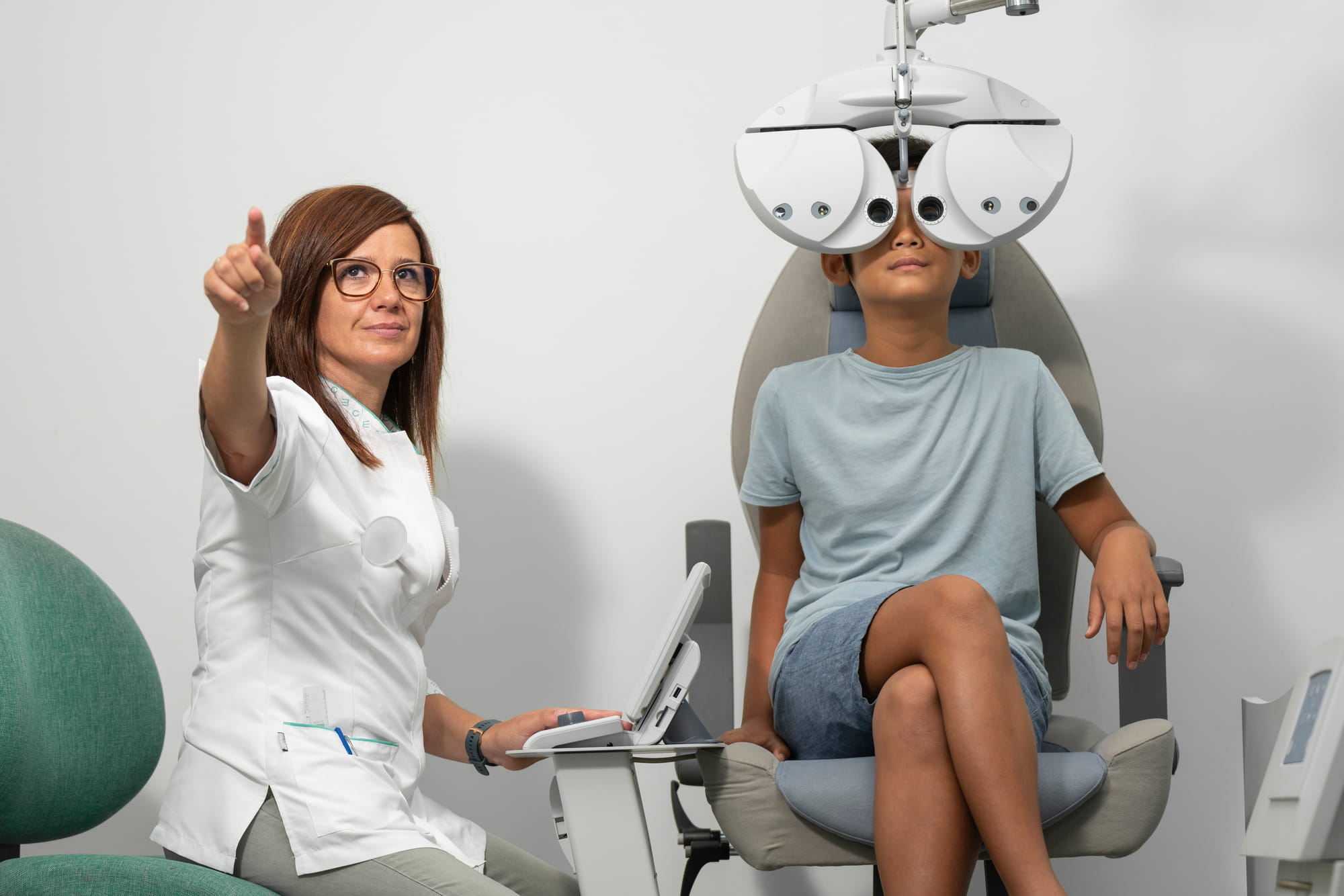 Young Asian boy with a modern phoropter at an optometrist consultation with an optometrist woman.
