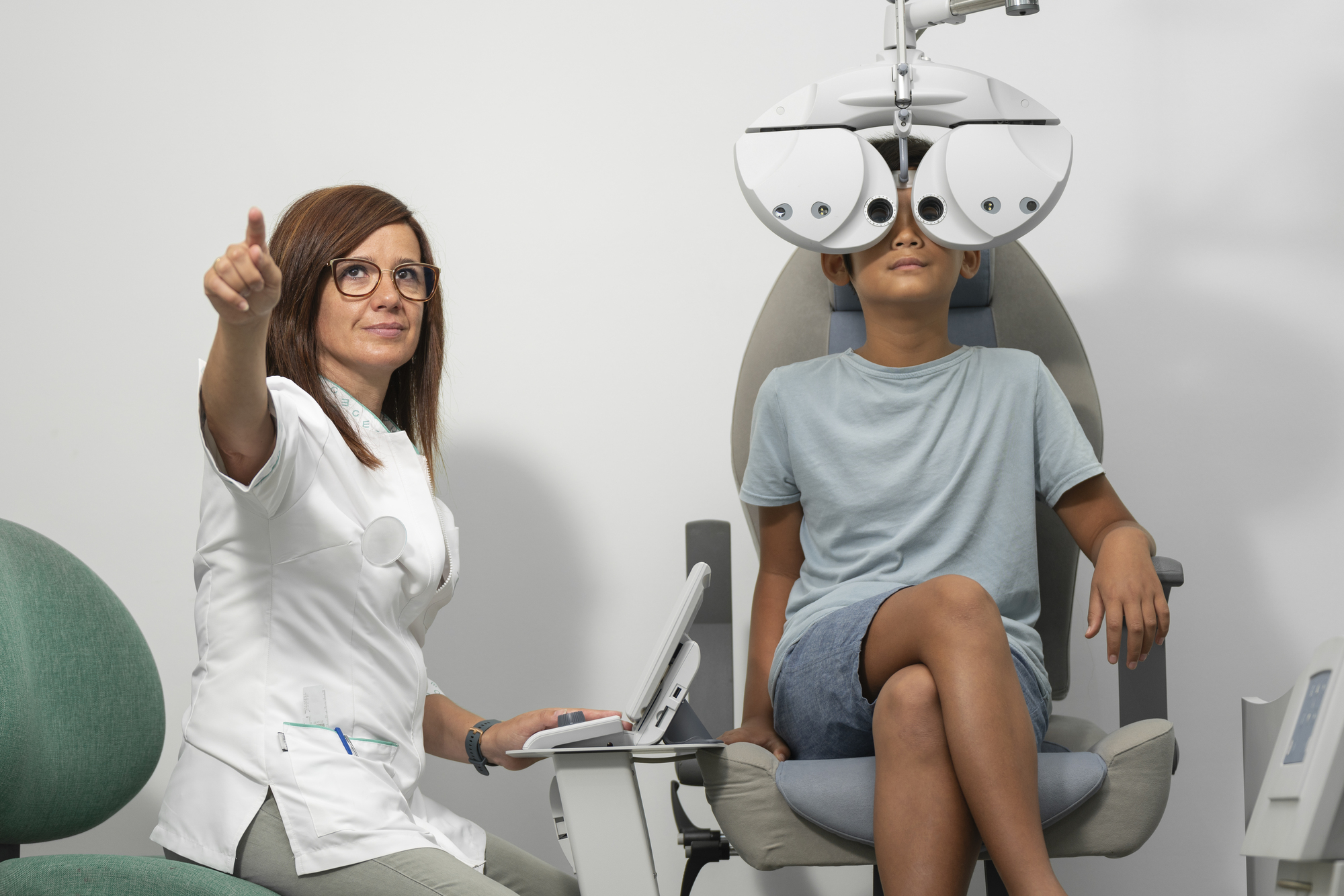 Young Asian boy with a modern phoropter at an optometrist consultation with an optometrist woman.