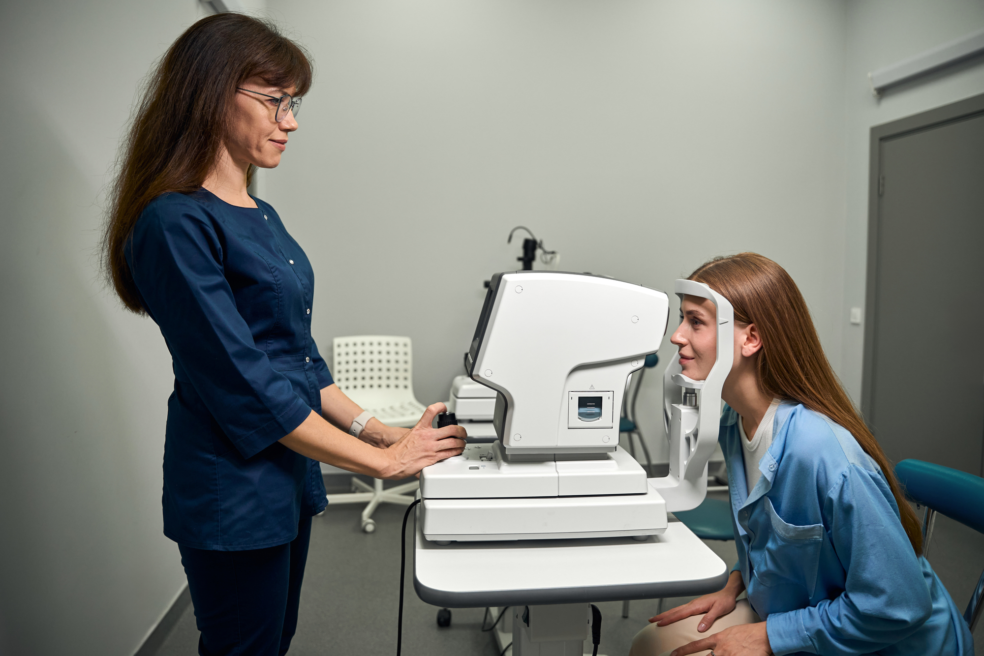 Female optometrist guides the patient into the correct position in front of the eye scanning device for accurate results