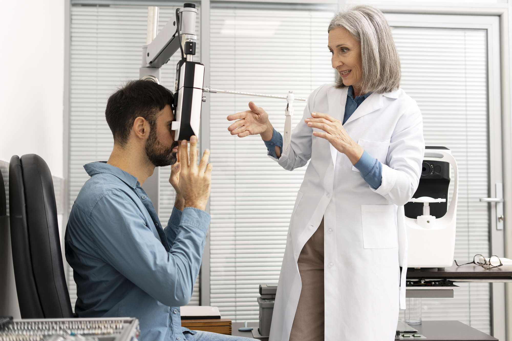 Senior female ophthalmologist is performing an eye examination on a male patient using a phoropter, adjusting the lenses and guiding him through the process in a modern eye clinic. Medical concept