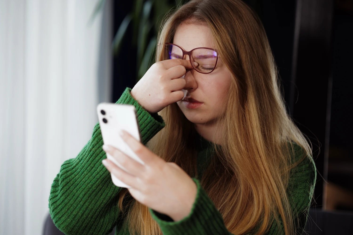 A young woman having eye strain when looking at her phone