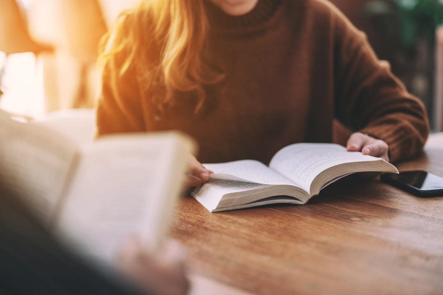 Close up of two people sitting and reading books together at a wooden table